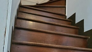 Un escalier en bois, doté d’une rampe et bordé d’un mur blanc d’un côté.