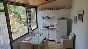 Une petite cuisine avec un coin repas, un réfrigérateur et une fenêtre donnant sur un mur en pierre et de la verdure.