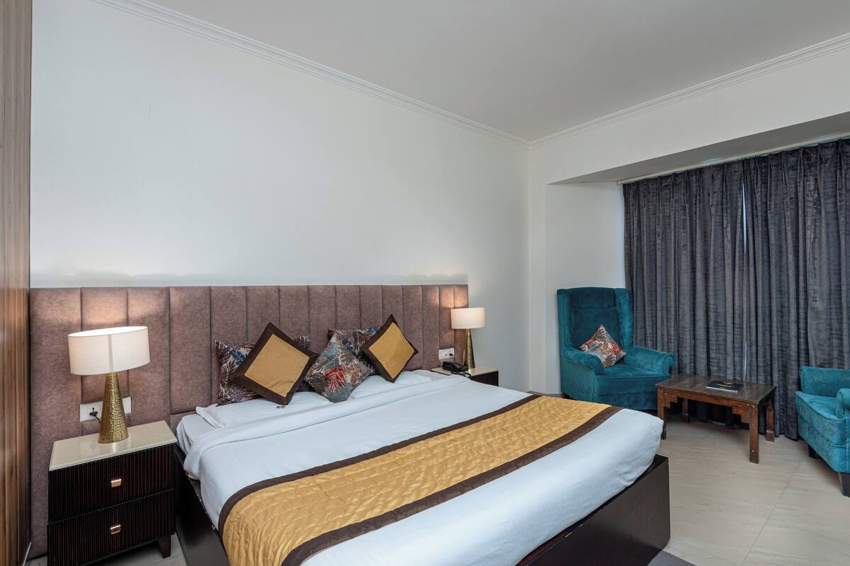 Una habitación de hotel con una cama grande, dos mesitas de noche con lámparas, una silla y una pequeña mesa.