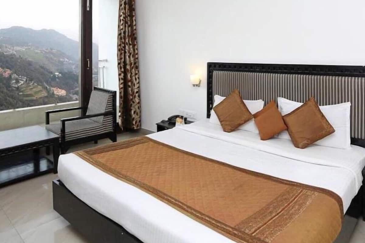 Una habitación de hotel con una cama, un escritorio, una silla, una mesita de noche, una lámpara y vistas a las montañas.
