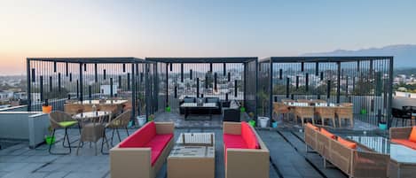 Una terraza en la azotea con mobiliario exterior, vistas a la ciudad y montañas al fondo.
