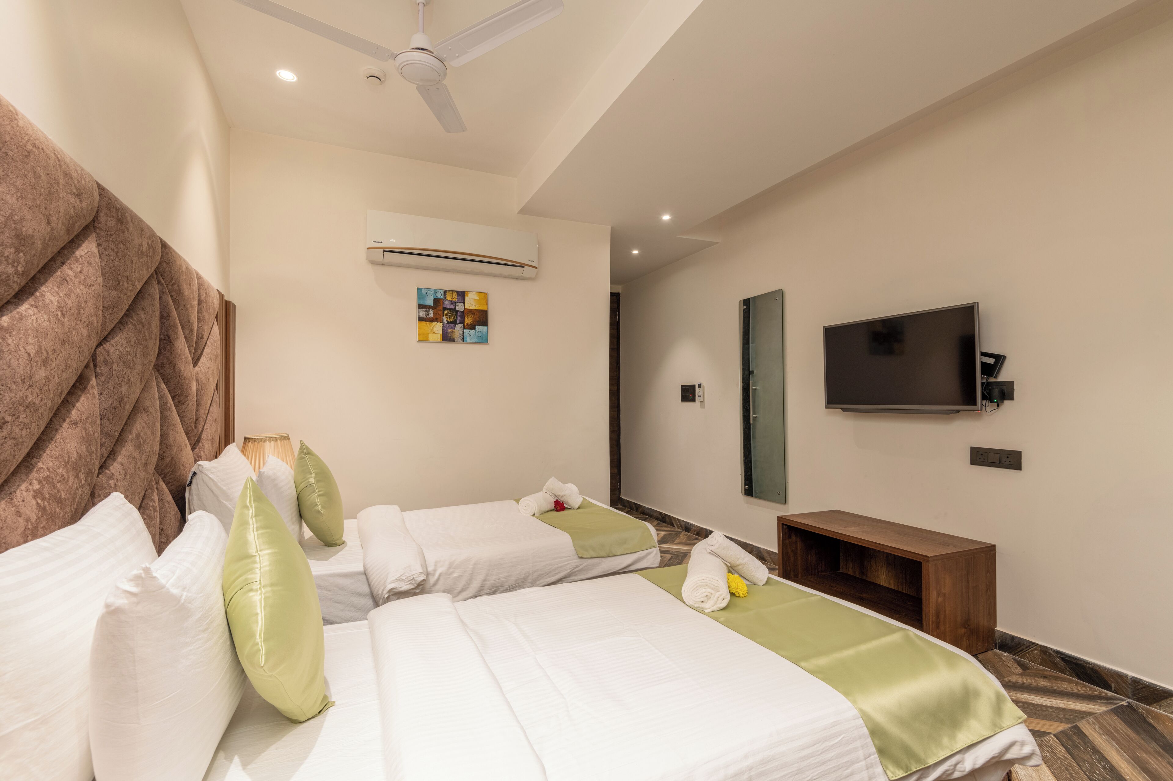 A hotel room with two beds, a television, a wooden bench, and an air conditioning unit.