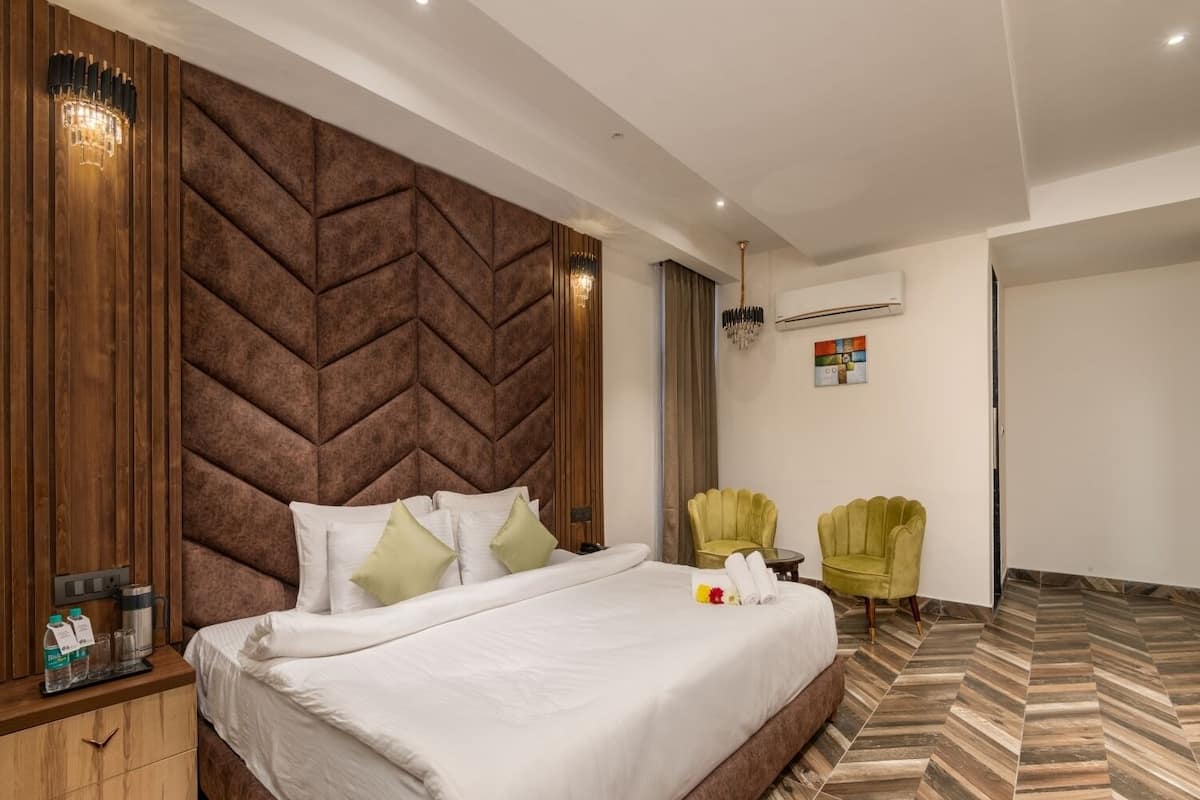 Moderni hotellihuone, jossa on suuri sänky, puinen pääty, puinen yöpöytä, kaksi vihreää nojatuolia ja kalanruotokuviollinen lattia.