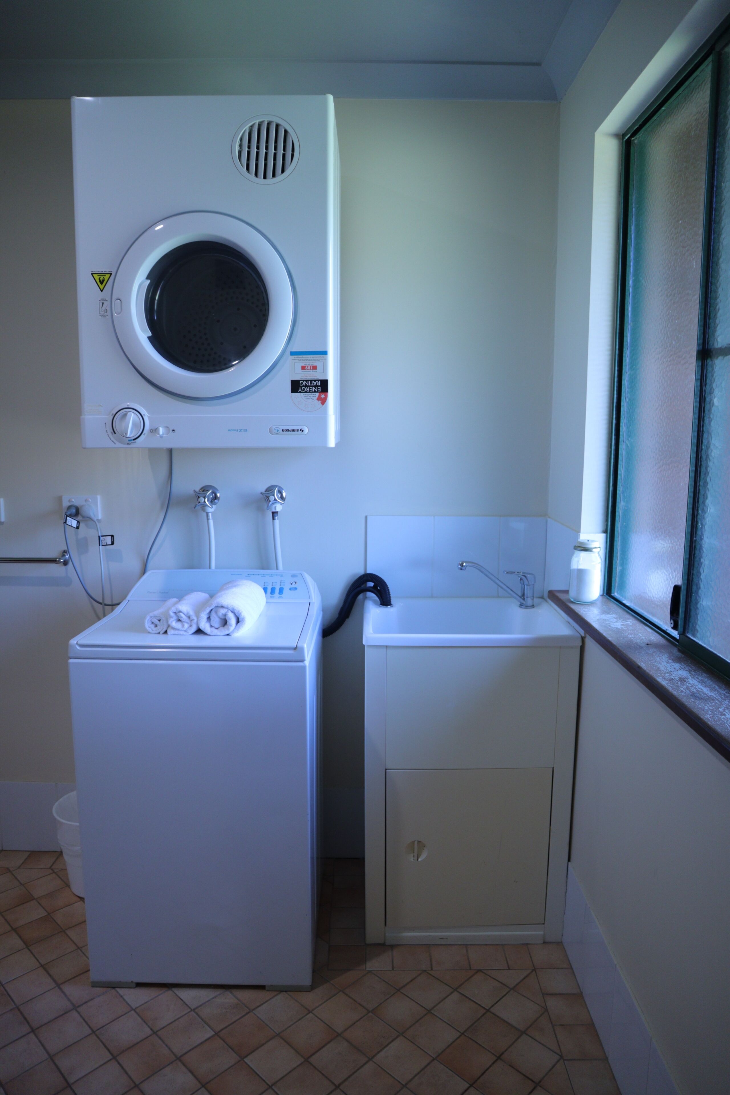 A laundry room with a front-loading washer and dryer, a sink, and a window.