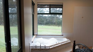 Un baño con bañera, ventana y vista a un área verde.