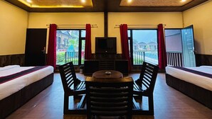 A hotel room with two beds, a TV, a table, and chairs. There are curtains and a balcony with a view. - MJ River Resort By DLS Hotels (Yamkeshwar)