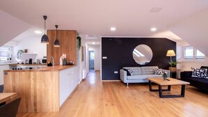 Un vaste espace de vie doté d’un plancher en bois, d’un canapé, d’une table basse et d’un coin cuisine avec un comptoir en bois et des luminaires suspendus.