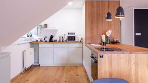 Une cuisine moderne avec des armoires blanches, un plan de travail en bois, un four encastré et un micro-ondes. Deux luminaires suspendus sont placés au-dessus de l’évier.