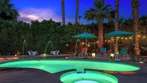 A swimming pool with a curved design, surrounded by palm trees and lounge chairs under umbrellas.