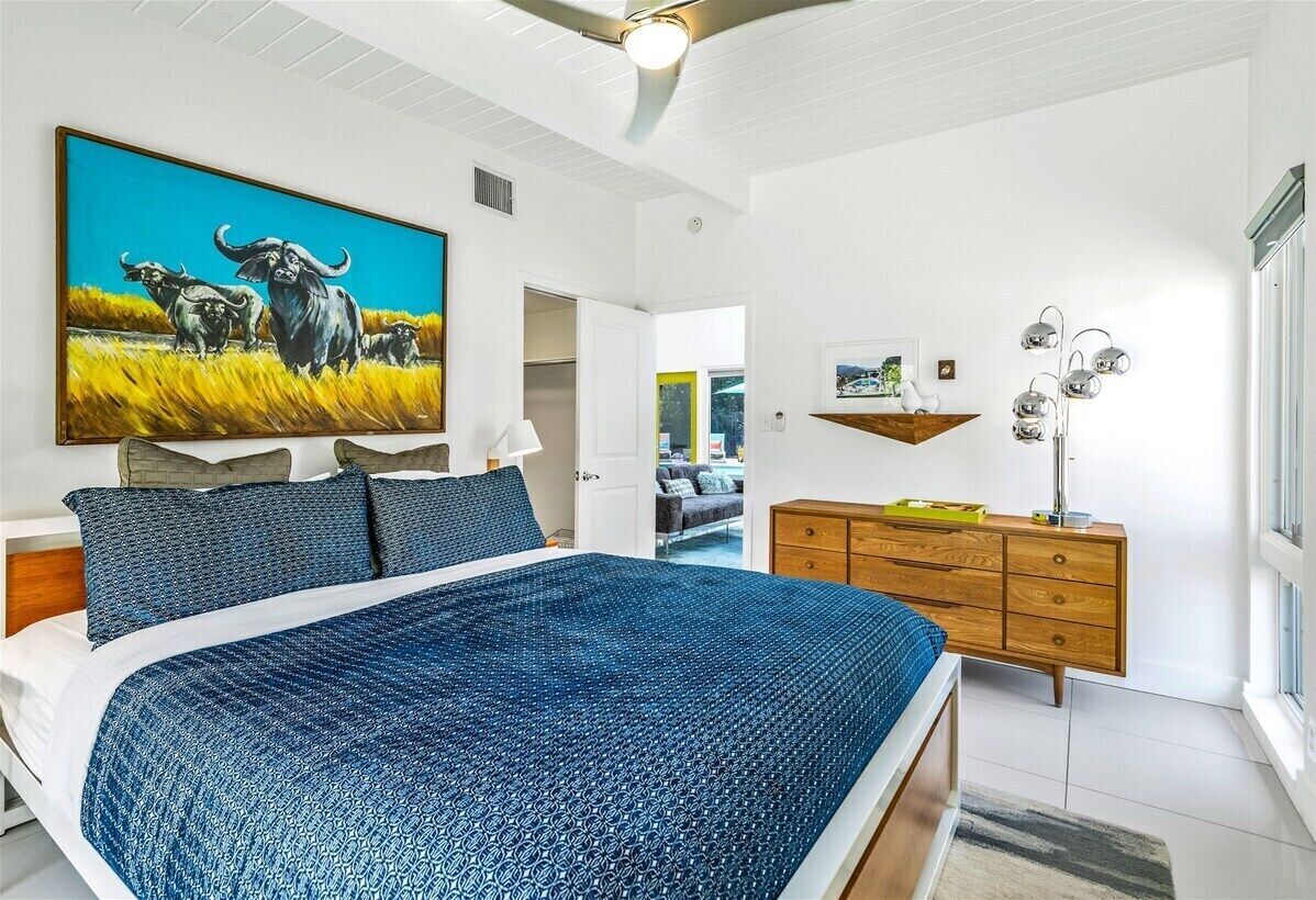 A bedroom with a bed, a painting, a dresser, and a ceiling fan.