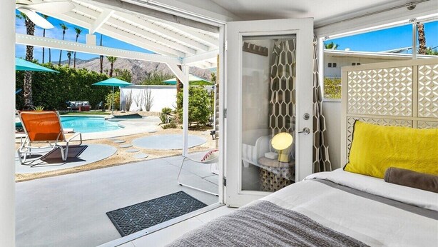 A bedroom with a bed, a nightstand, and a view of a swimming pool and patio area.
