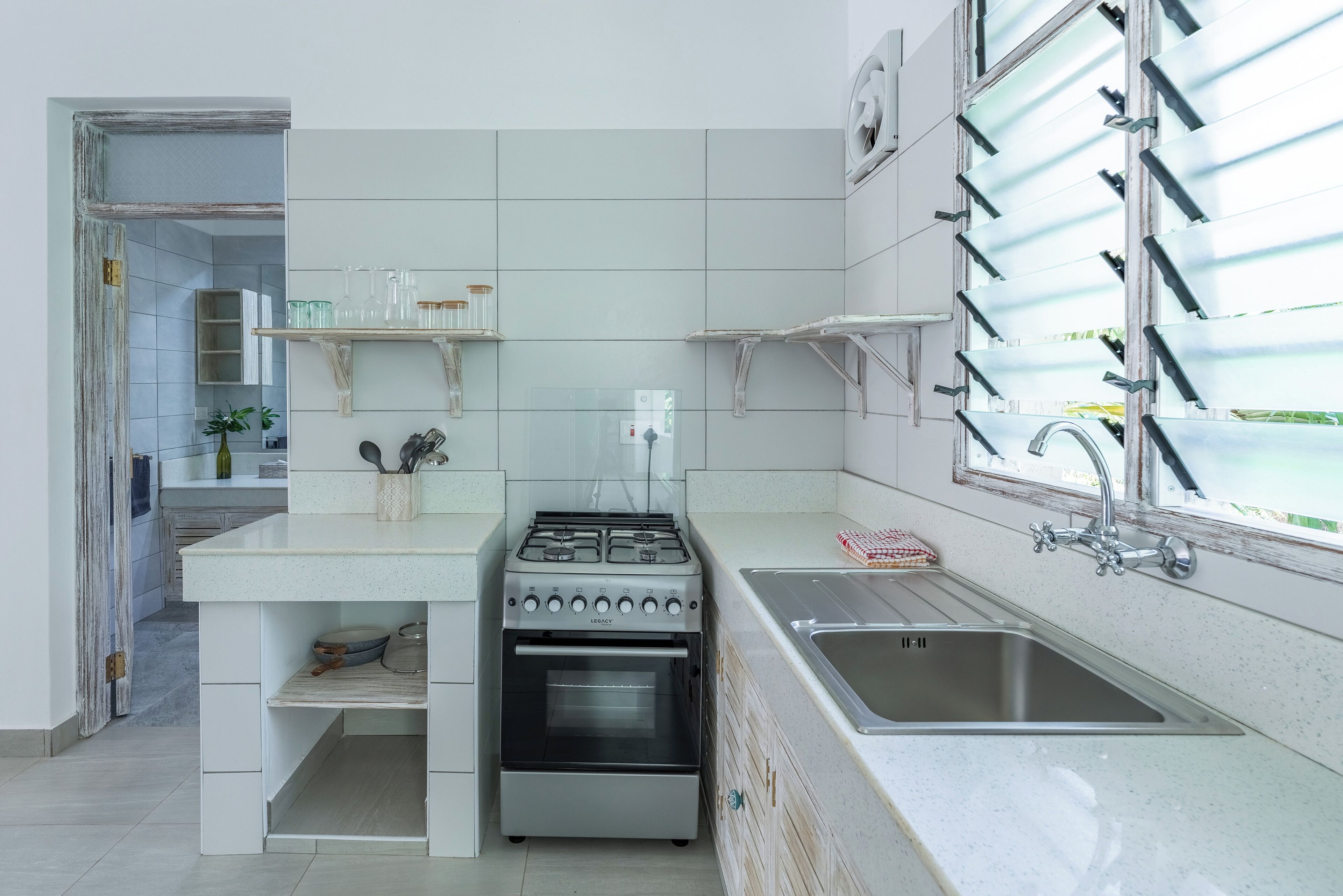 A compact kitchen with white cabinetry, a gas stove, a sink, and a window with blinds.