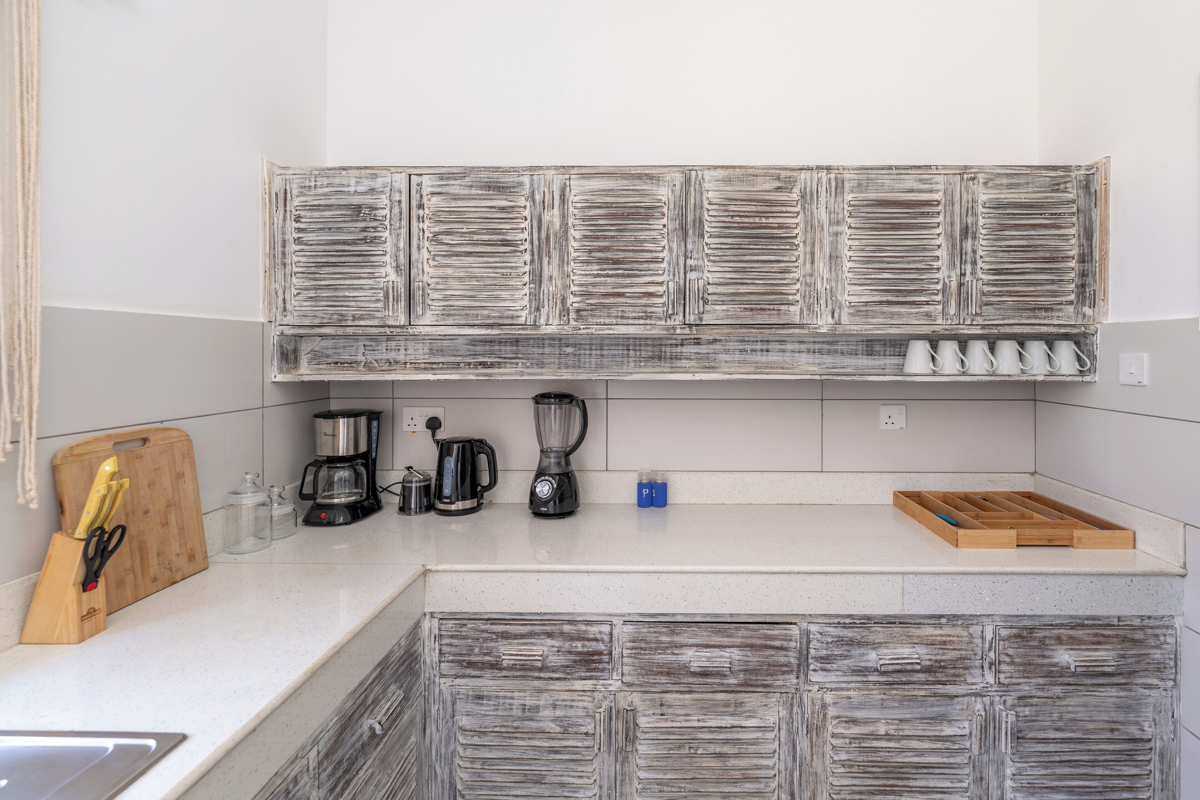 A kitchen with a rustic wooden cabinet, a coffee maker, a blender, and a wooden cutting board with utensils.