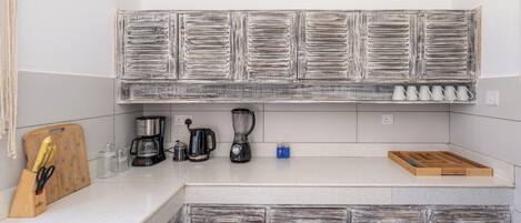 A kitchen with a rustic wooden cabinet, a coffee maker, a blender, and a wooden cutting board with utensils.