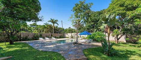 A backyard with a stone pathway, a swimming pool, and lounge chairs.