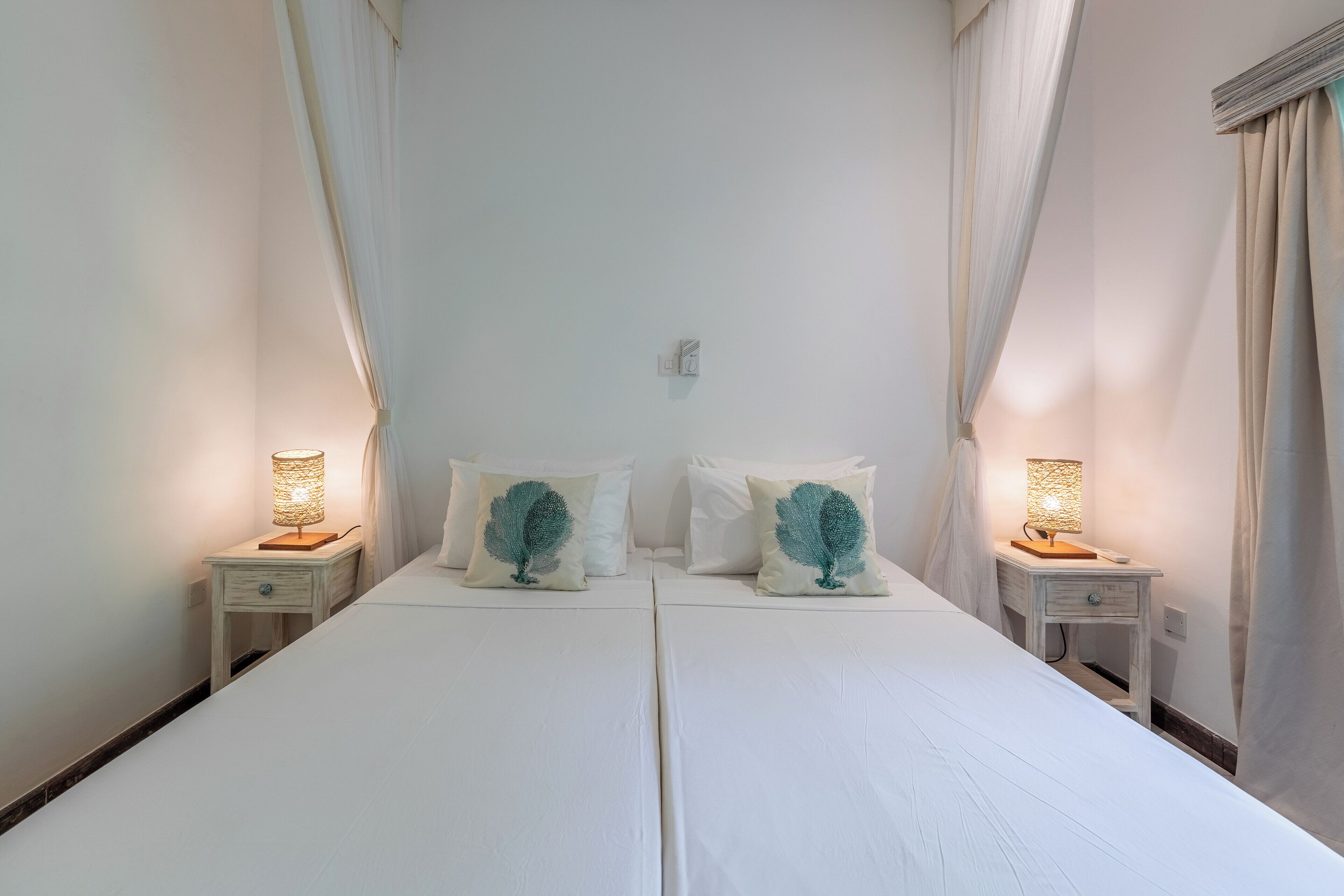Un lit double avec du linge de lit blanc, deux tables de chevet avec des lampes et des coussins décoratifs.
