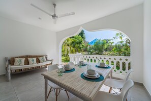 A dining area with a wooden table set for four, white chairs, and a white sofa with cushions. - Hibiscus (Diani Beach)