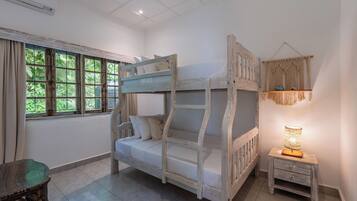 Una cama litera con una mesita de noche y una decoración de macramé colgante en una habitación con un ventanal grande.