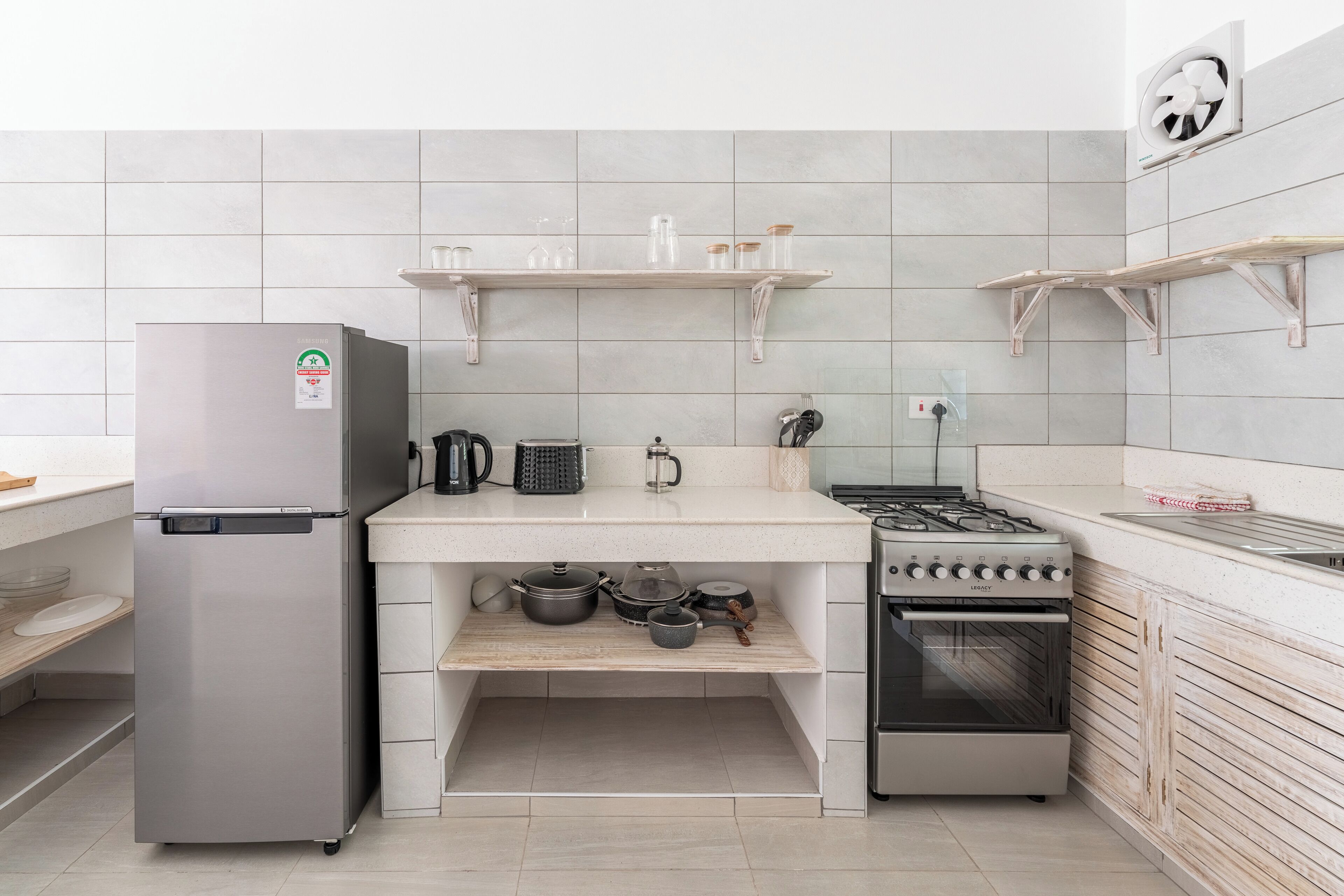 A modern kitchen with a stainless steel refrigerator, a gas stove, and wooden shelves.