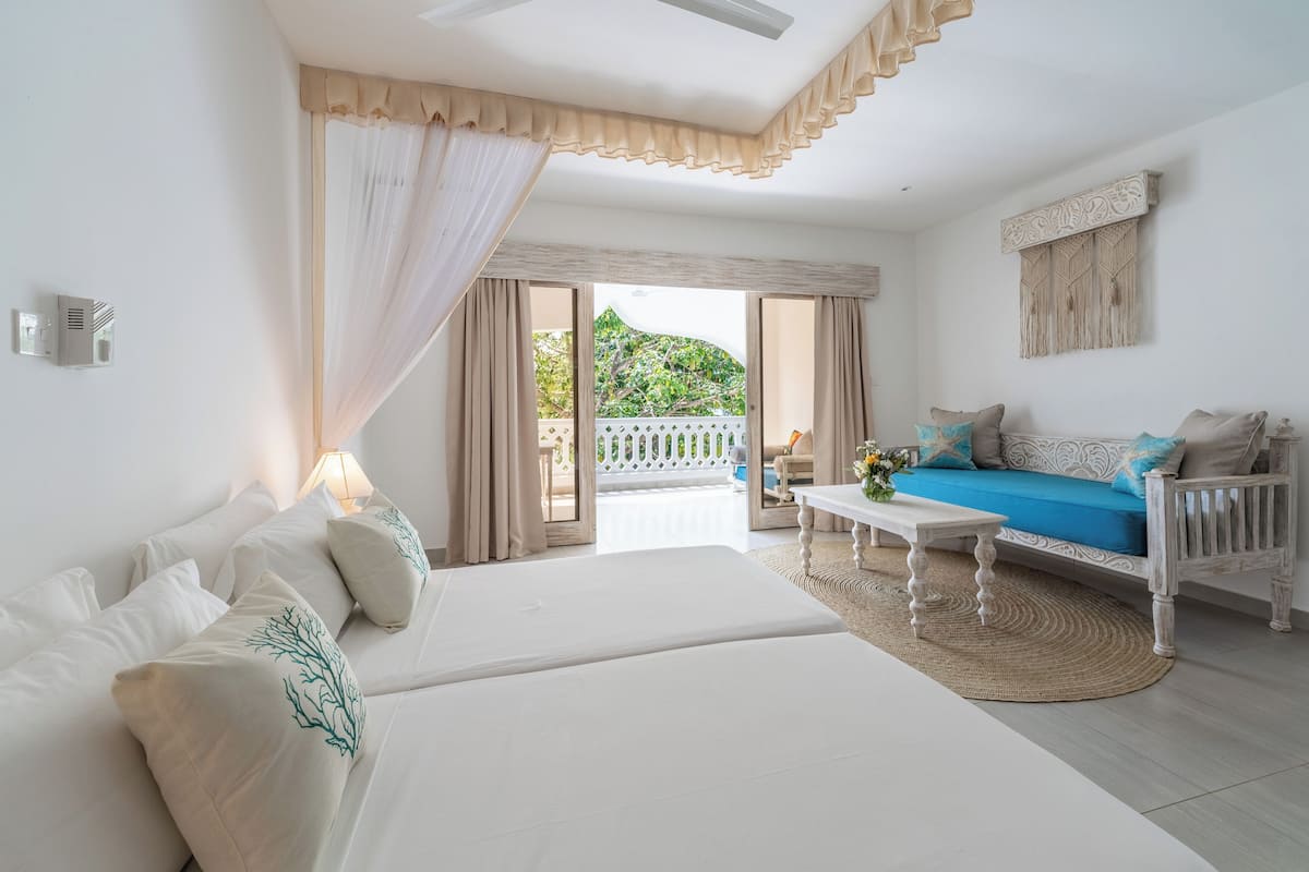 A bedroom with a large bed, a sofa, a coffee table, and a view of the outdoors.