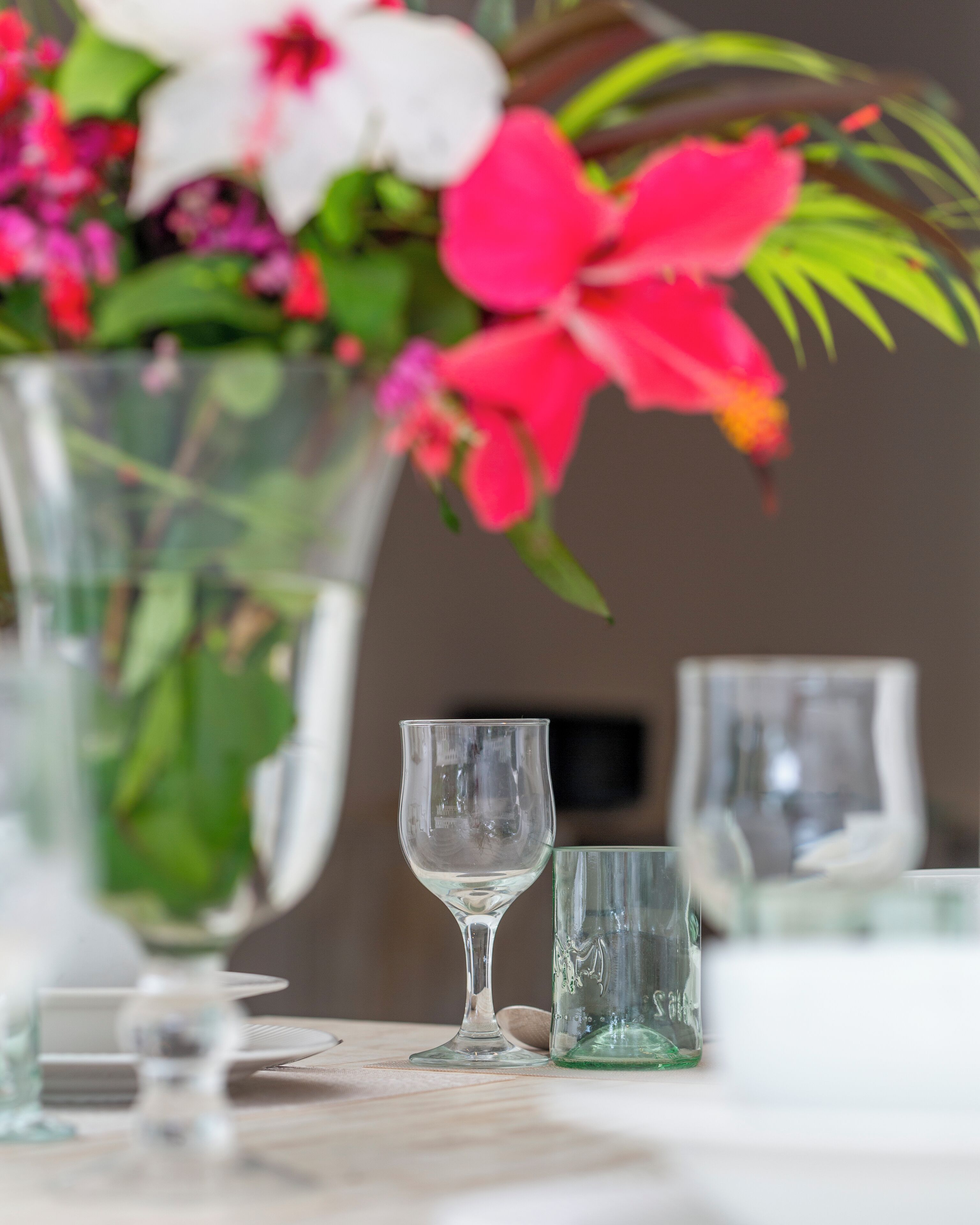 A table with a clear glass vase containing flowers, two clear stemmed glasses, and a green glass.