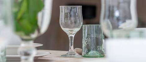 A table with a clear glass vase containing flowers, two clear stemmed glasses, and a green glass.