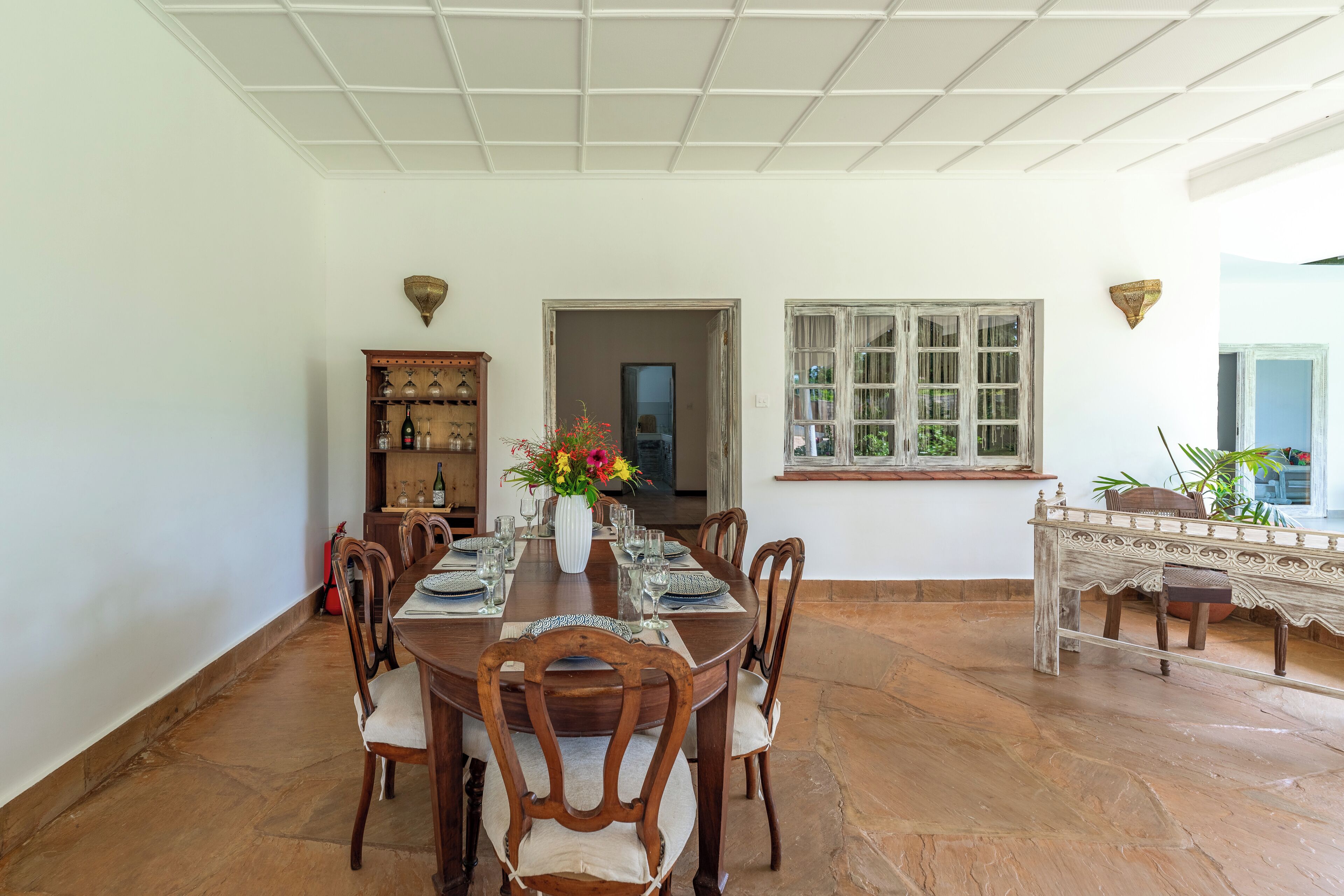 Un comedor con una larga mesa de madera dispuesta para seis personas, rodeada por seis sillas. Un jarrón con flores se encuentra en el centro.