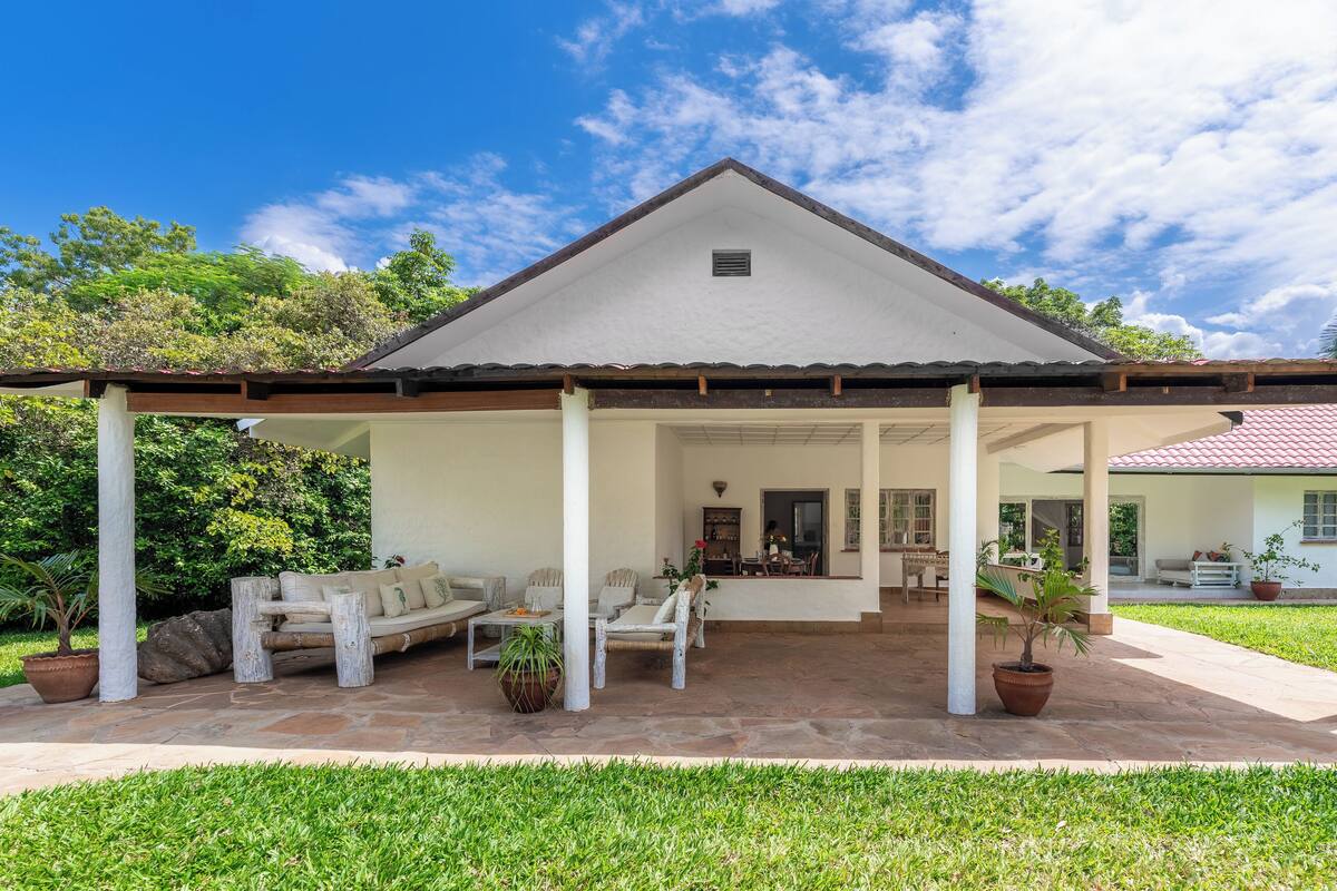 A covered outdoor seating area with stone flooring, white walls, and a red-tiled roof.