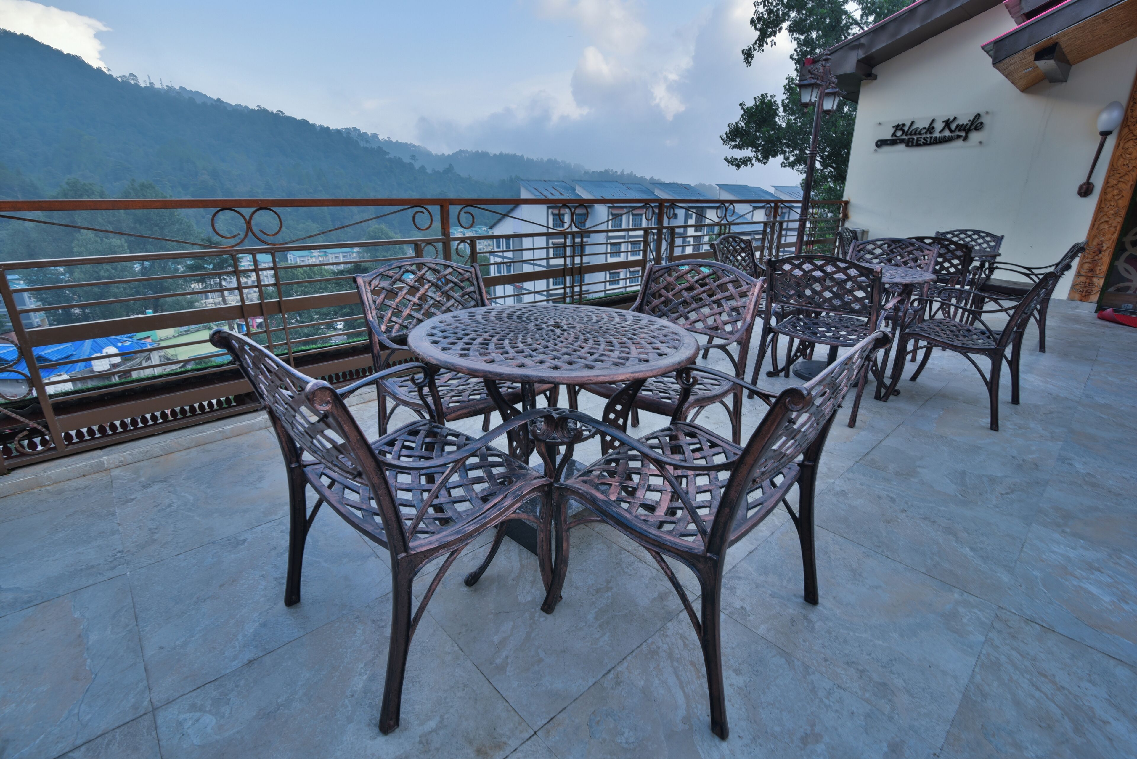 Une terrasse avec des tables rondes et des chaises en osier, offrant une vue sur un paysage montagneux.
