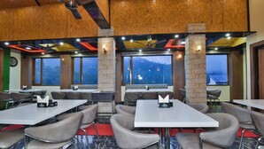 A restaurant with multiple tables and chairs, large windows with a mountain view, and a ceiling fan.