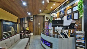 A reception area with a wooden ceiling, a reception desk with a computer, a seating area with a sofa, and framed certificates on the wall.