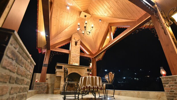 A covered outdoor patio with a fireplace, a table with chairs, and a chandelier.