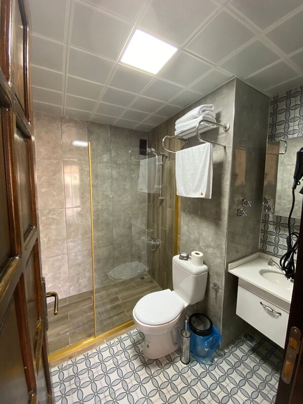 Un baño con ducha envuelta en vidrio, inodoro, lavamanos y espejo.