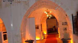 Uma entrada em arco com um tapete vermelho que leva a um salão, uma planta em vaso e uma câmera de segurança.