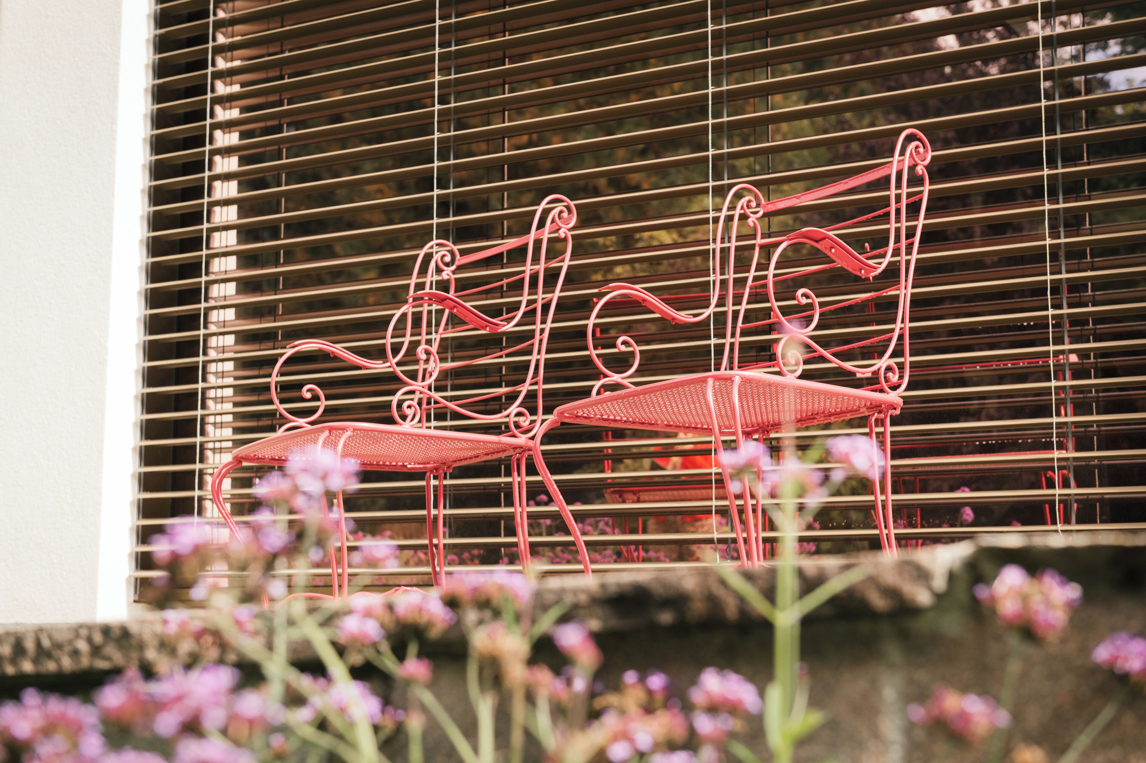 A metal bench with a curved design, positioned in front of a window with horizontal blinds.