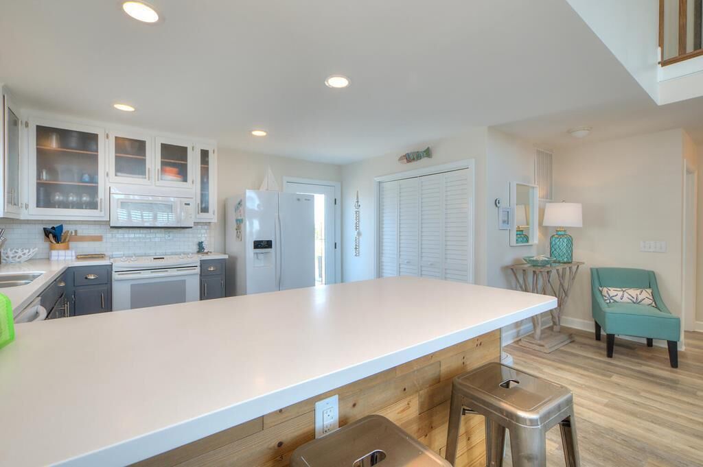 Una cuina moderna amb armaris blancs, una illa gran i una cadira color turquesa.