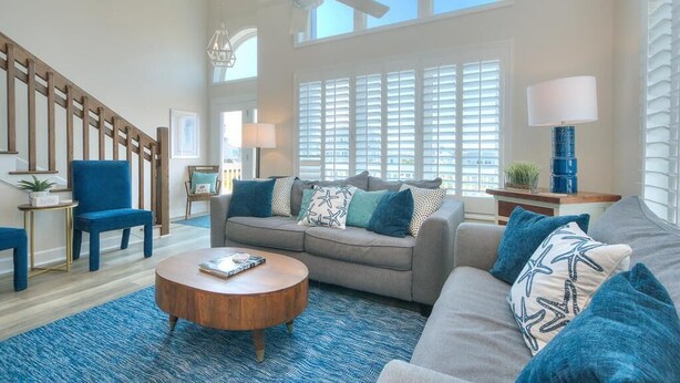 A spacious living room with a staircase, a ceiling fan, and large windows. - Discover Blue Dolphin in Oak Island: a spacious 5-bedroom oceanview home for 12! (Oak Island)