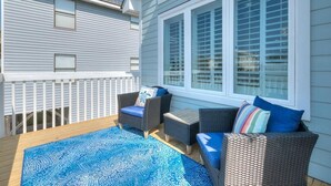 A covered deck with outdoor furniture, a window with blinds, and a white fence. - Discover Blue Dolphin in Oak Island: a spacious 5-bedroom oceanview home for 12! (Oak Island)
