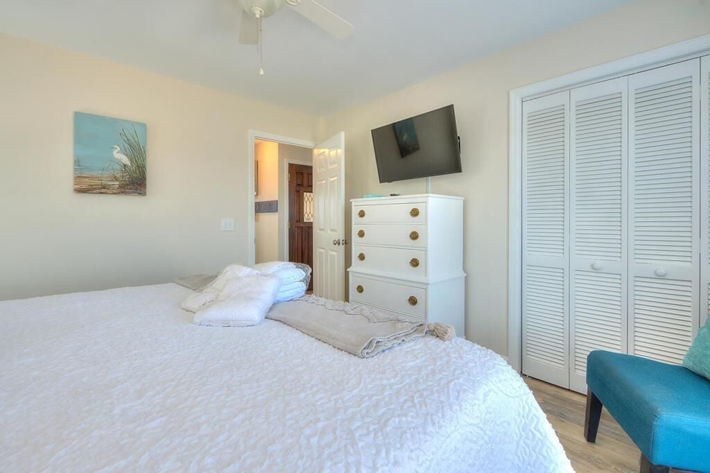 A bedroom with a large bed, a TV mounted on the wall, a white dresser, and a closet with louvered doors.