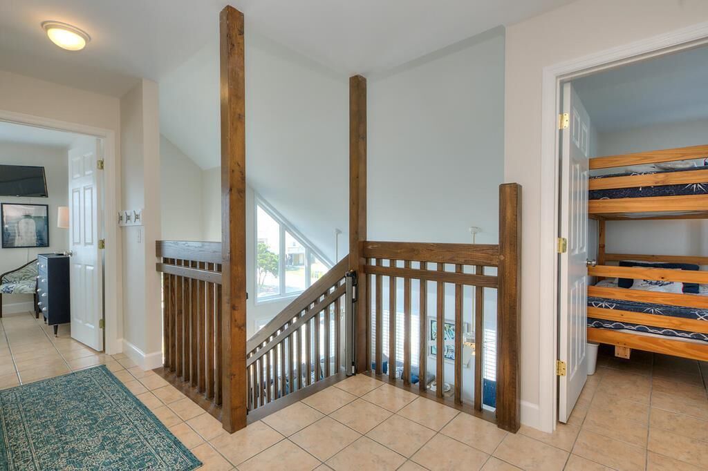 Una escalera con barandillas de madera, vista al exterior y una cama litera en la habitación contigua.