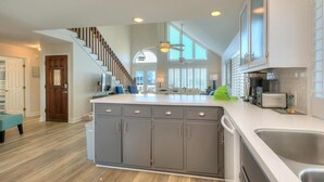 A modern kitchen with a large island, grey cabinets, and a staircase leading to an upper level. - Discover Blue Dolphin in Oak Island: a spacious 5-bedroom oceanview home for 12! (Oak Island)