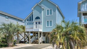 A two-story beachfront house with a balcony, palm trees, and a clear sky. - Discover Blue Dolphin in Oak Island: a spacious 5-bedroom oceanview home for 12! (Oak Island)