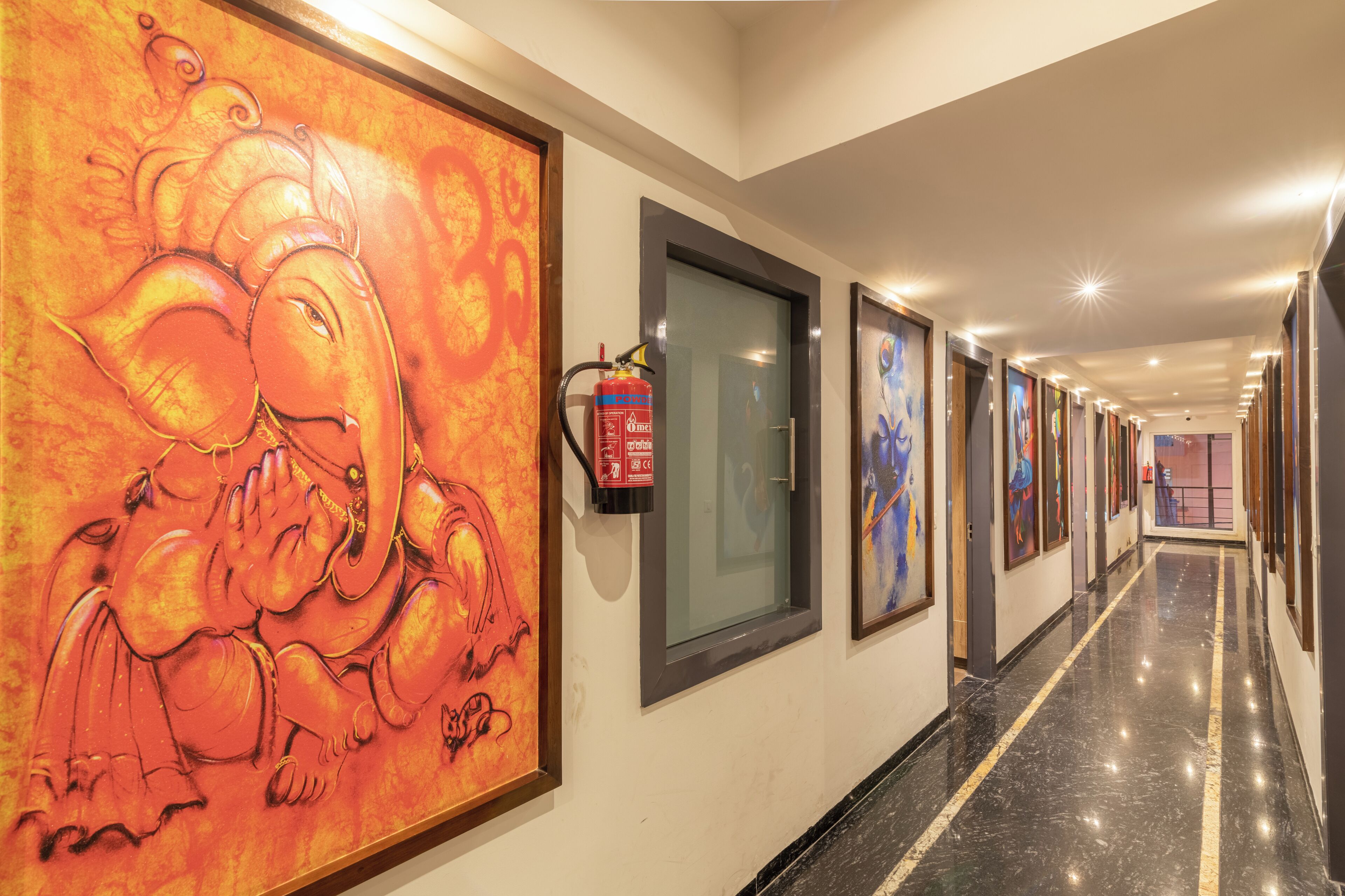 Un pasillo de hotel con obras de arte en las paredes, un extintor y un piso de mármol.