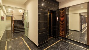 Een moderne hotel lobby met een marmeren vloer, een trap en een grote spiegel die de lift weerspiegelt.