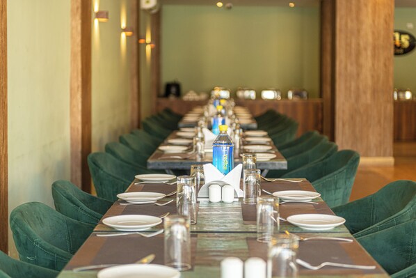 A long dining table set with green upholstered chairs, clear glassware, and neatly arranged plates and cutlery.
