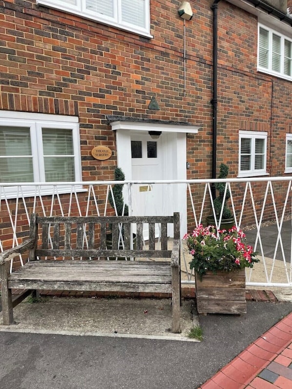 Un bâtiment en briques avec une porte blanche, un banc et un pot de fleurs.