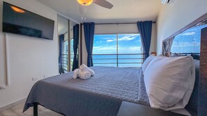 Ein Schlafzimmer mit Bett, Deckenventilator, Fernseher und Meerblick.
