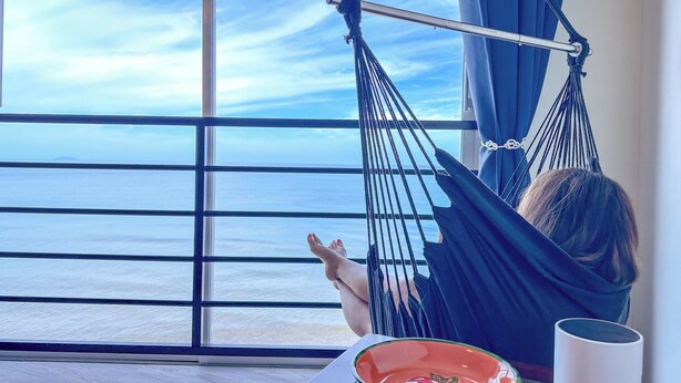 Ein Hängestuhl neben einem großen Fenster mit Blick auf das Meer.