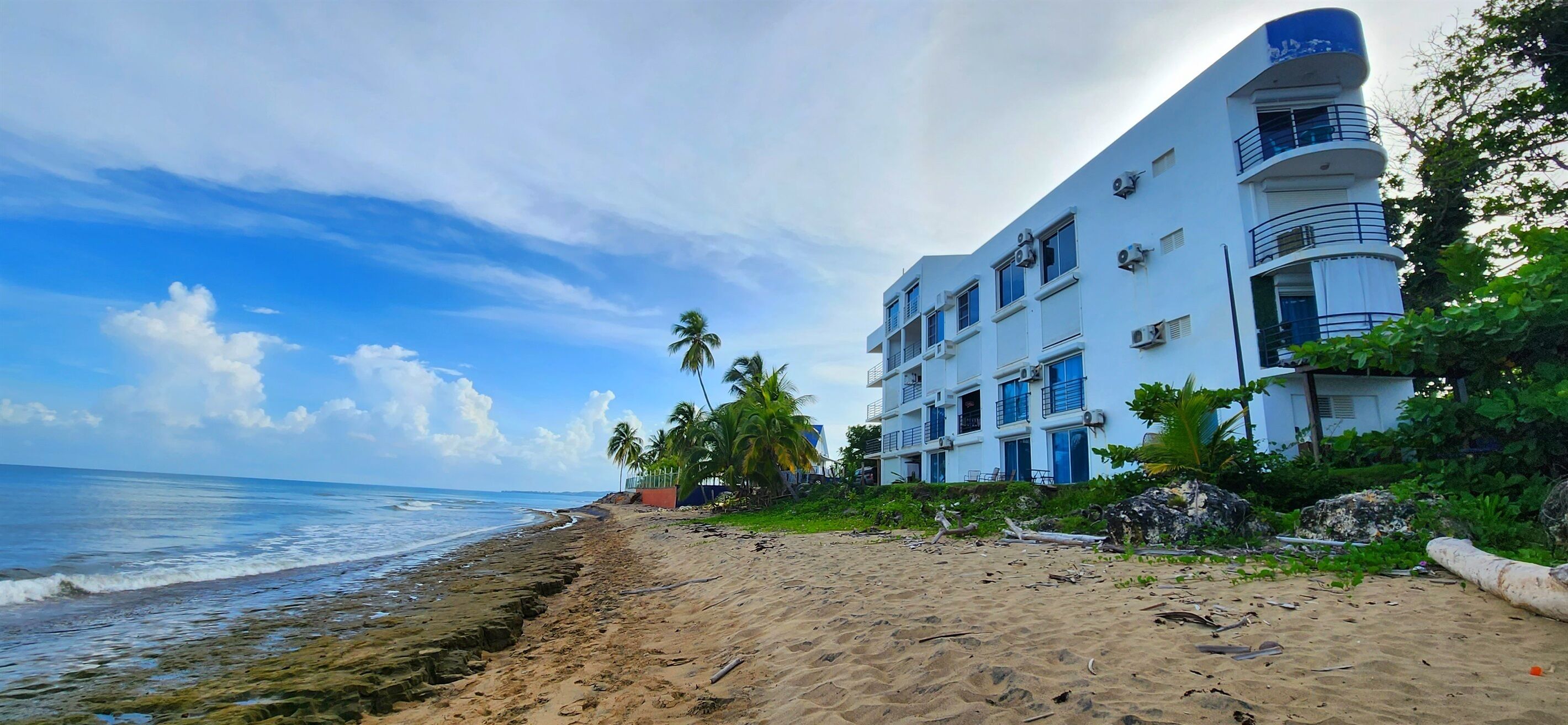 Een strandhotel met meerdere balkons, een zandstrand en palmbomen.
