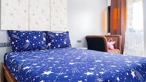 Un dormitorio con una cama, una silla, un papel tapiz floral en la pared y una ventana con cortinas.